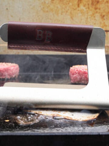 Smashing a burger patty with a burger press for smash burgers on the griddle