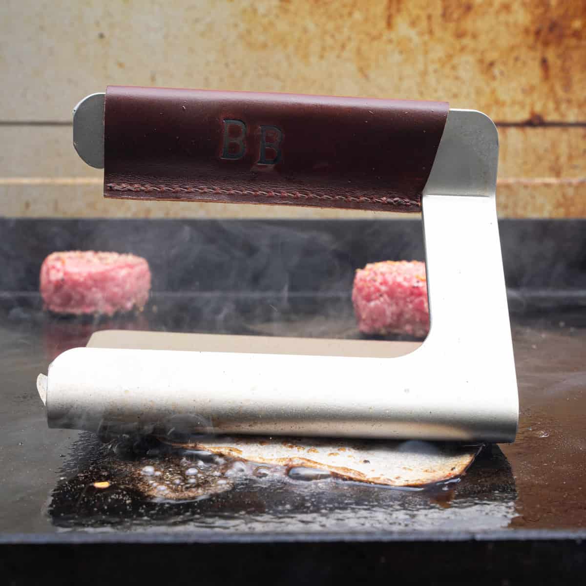 Smashing a burger patty with a burger press for smash burgers on the griddle