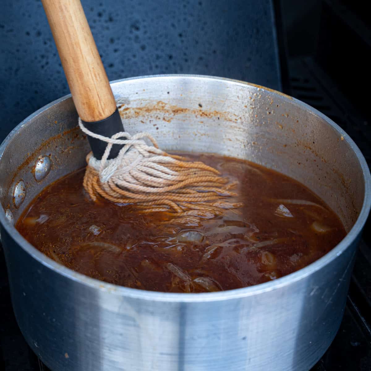Stirring a mop sauce with a bbq mop in the final stages of cooking