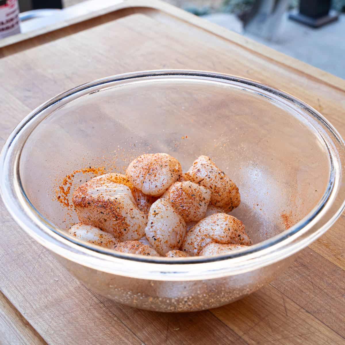 Fresh scallops being seasoned with creole seasoning and oil in a bowl