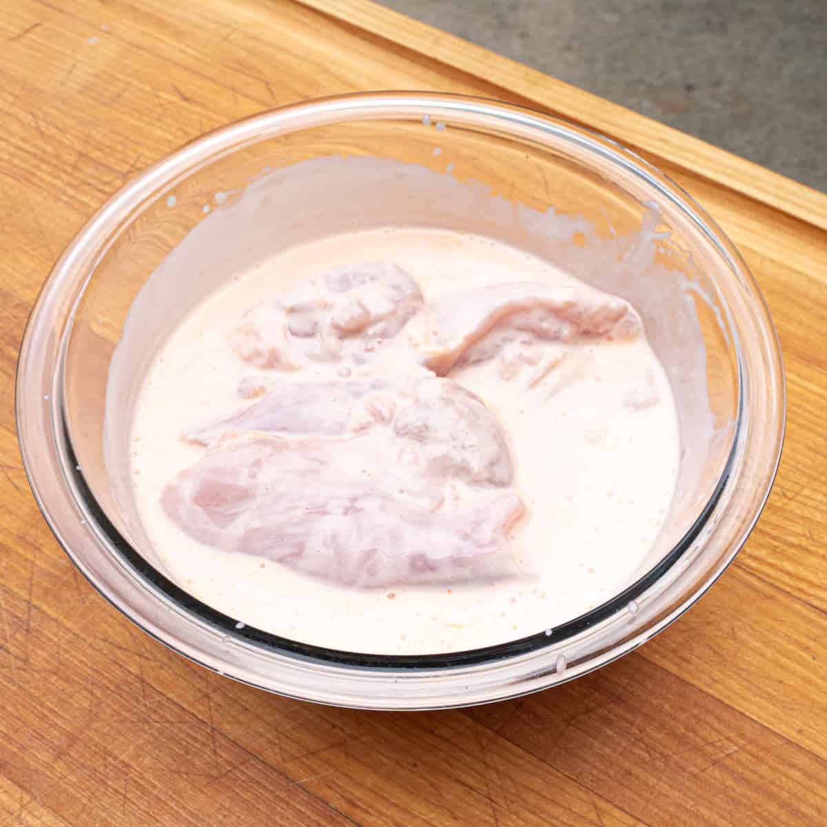 Chicken thighs marinating in buttermilk and hot sauce mixture