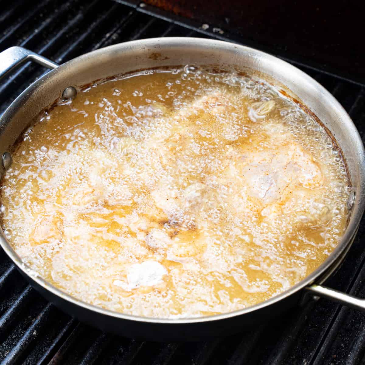 Chicken recently placed in a frying skillet to fry
