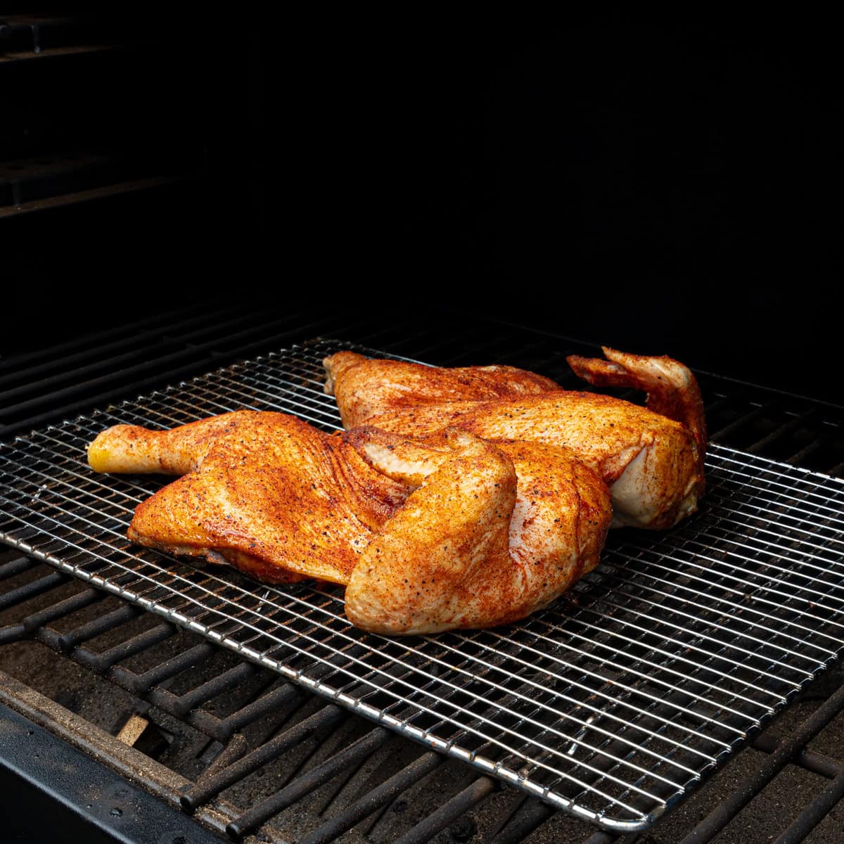Spatchcock chicken smoking on a pellet grill and about to be brushed with BBQ sauce
