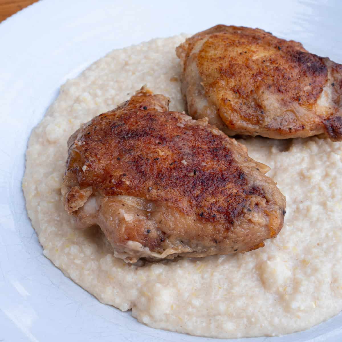 Pan seared chicken thighs served over grits ready to be smothered with chicken gravy