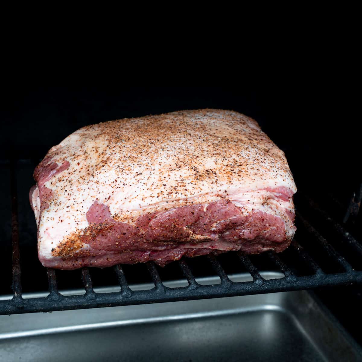 Seasoned pork butt recently placed on the smoker