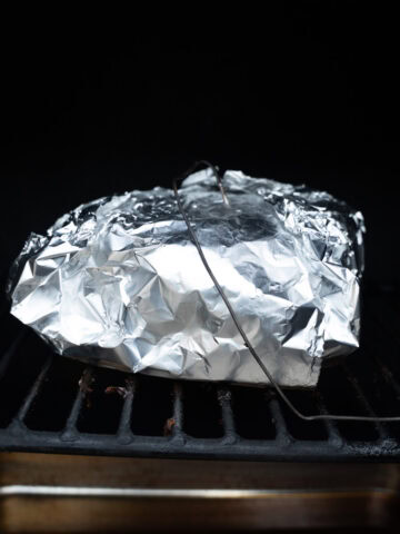 Pork shoulder wrapped in aluminum foil and placed on the smoker