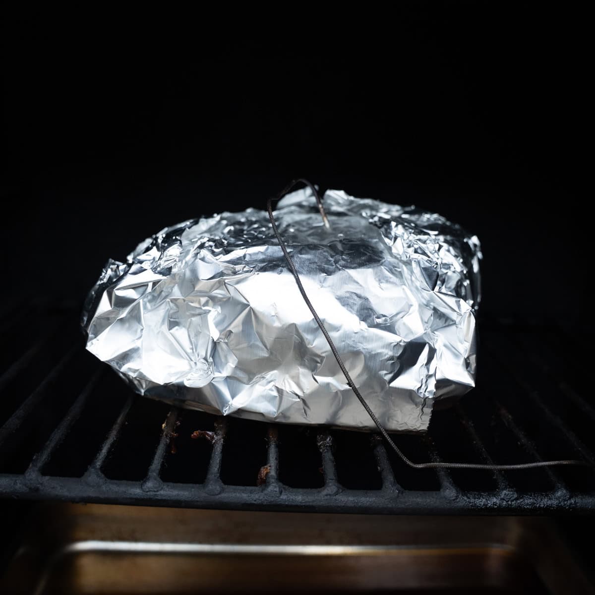 Pork shoulder wrapped in aluminum foil and placed on the smoker